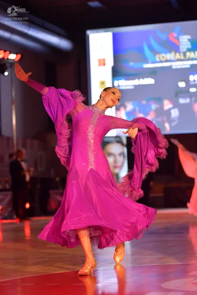 Dancesport competitor: Female dancer: vibrant pink ballroom dress with a sequined bodice, long sleeves 