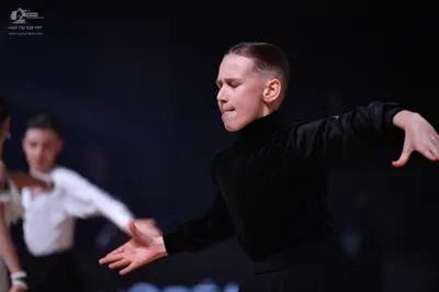 Dancesport competitor: Foreground male dancer: black long-sleeved turtleneck shirt and black trousers