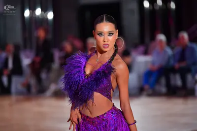 Dancesport competitor: Female dancer: purple Latin dance costume featuring a sequined crop top with lar