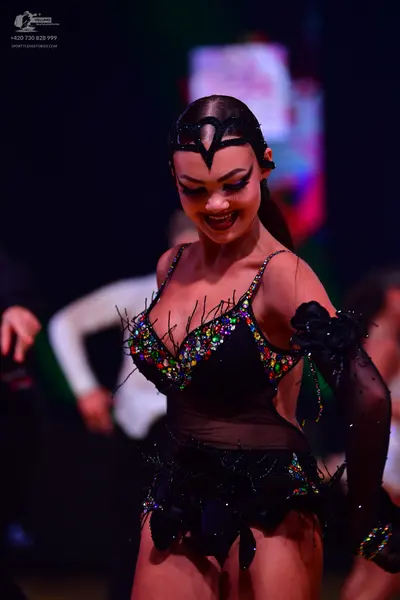 Dancesport competitor: Female dancer: black Latin costume with colorful sequins (green, blue, gold), sh