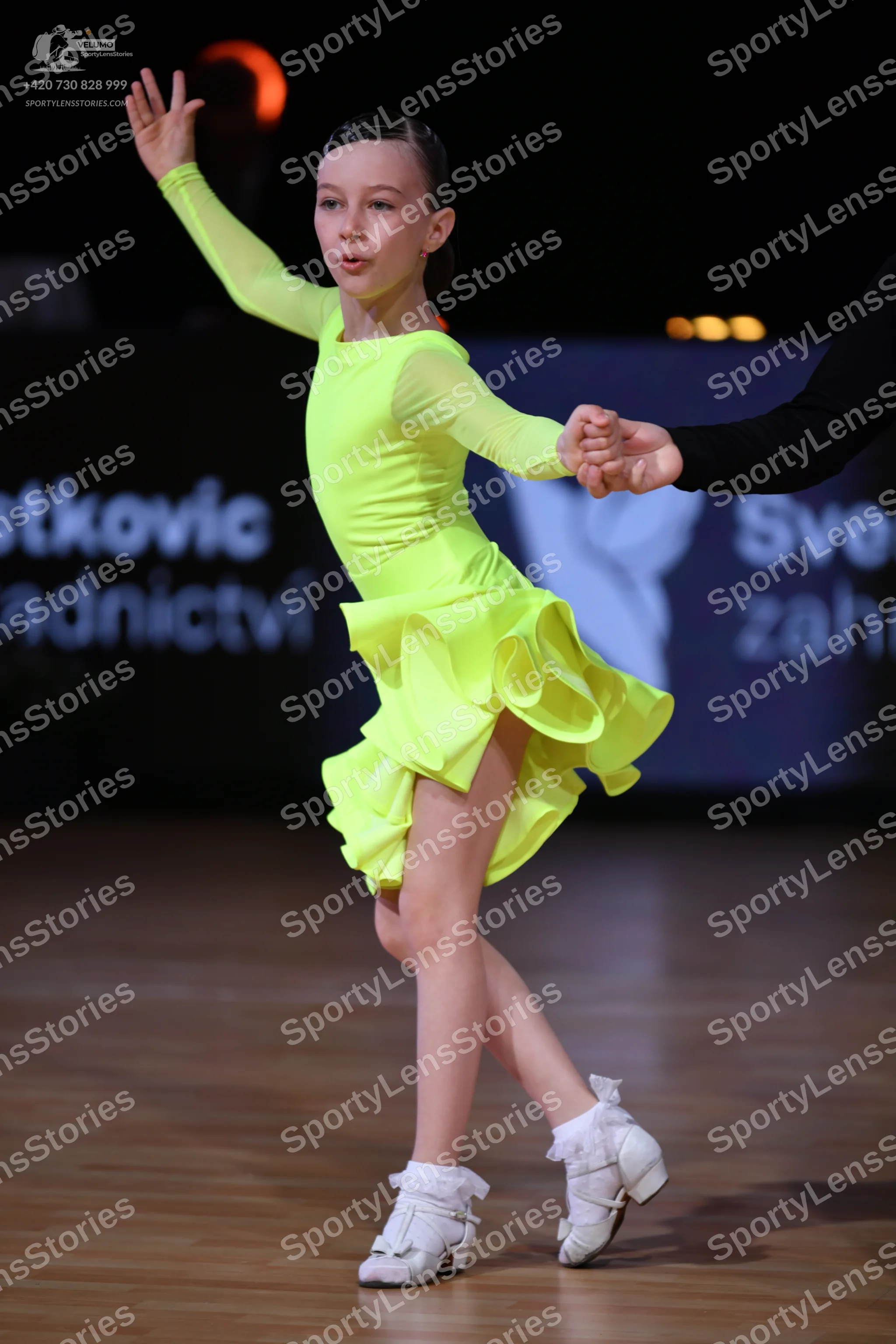 Dancesport competitor: Female dancer: neon yellow long-sleeved Latin dress with a ruffled skirt and whi