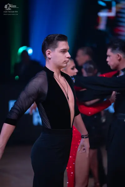 Dancesport competitor: Male dancer: black top with black mesh sleeves and side panels, black trousers, 