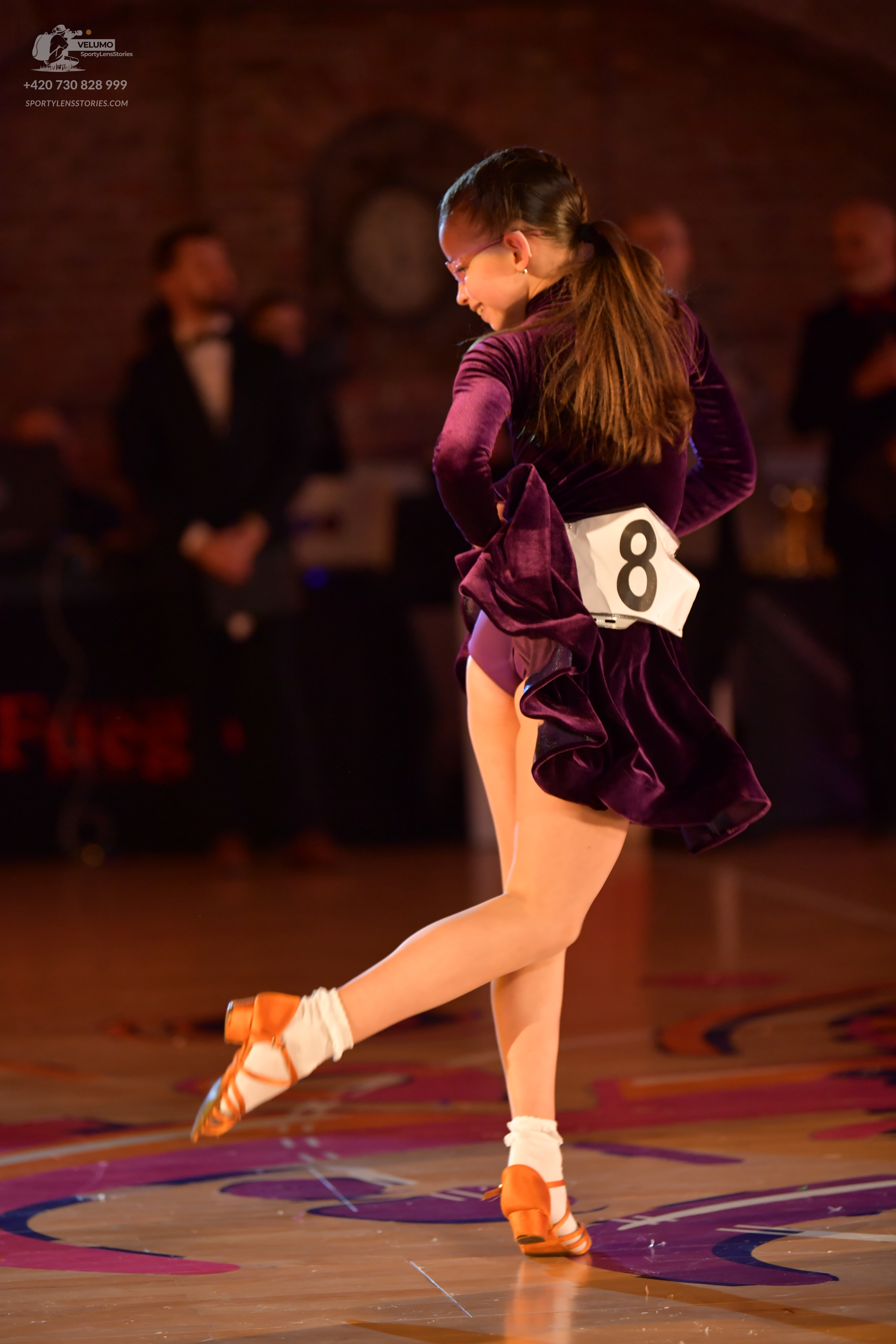 Dancesport competitor: Female dancer: dark purple velvet Latin dress with ruffles, white socks, and tan