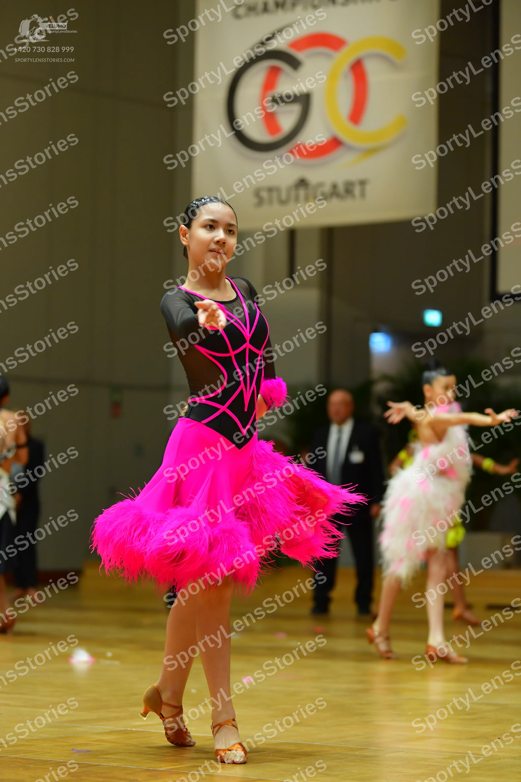 Dancesport competitor: Female dancer in foreground: black long-sleeved Latin dress with a bright pink g