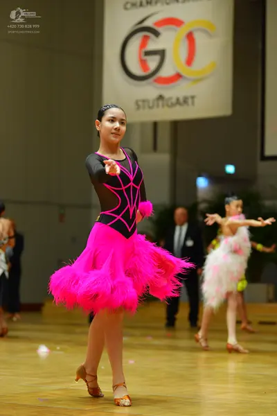 Dancesport competitor: Female dancer in foreground: black long-sleeved Latin dress with a bright pink g
