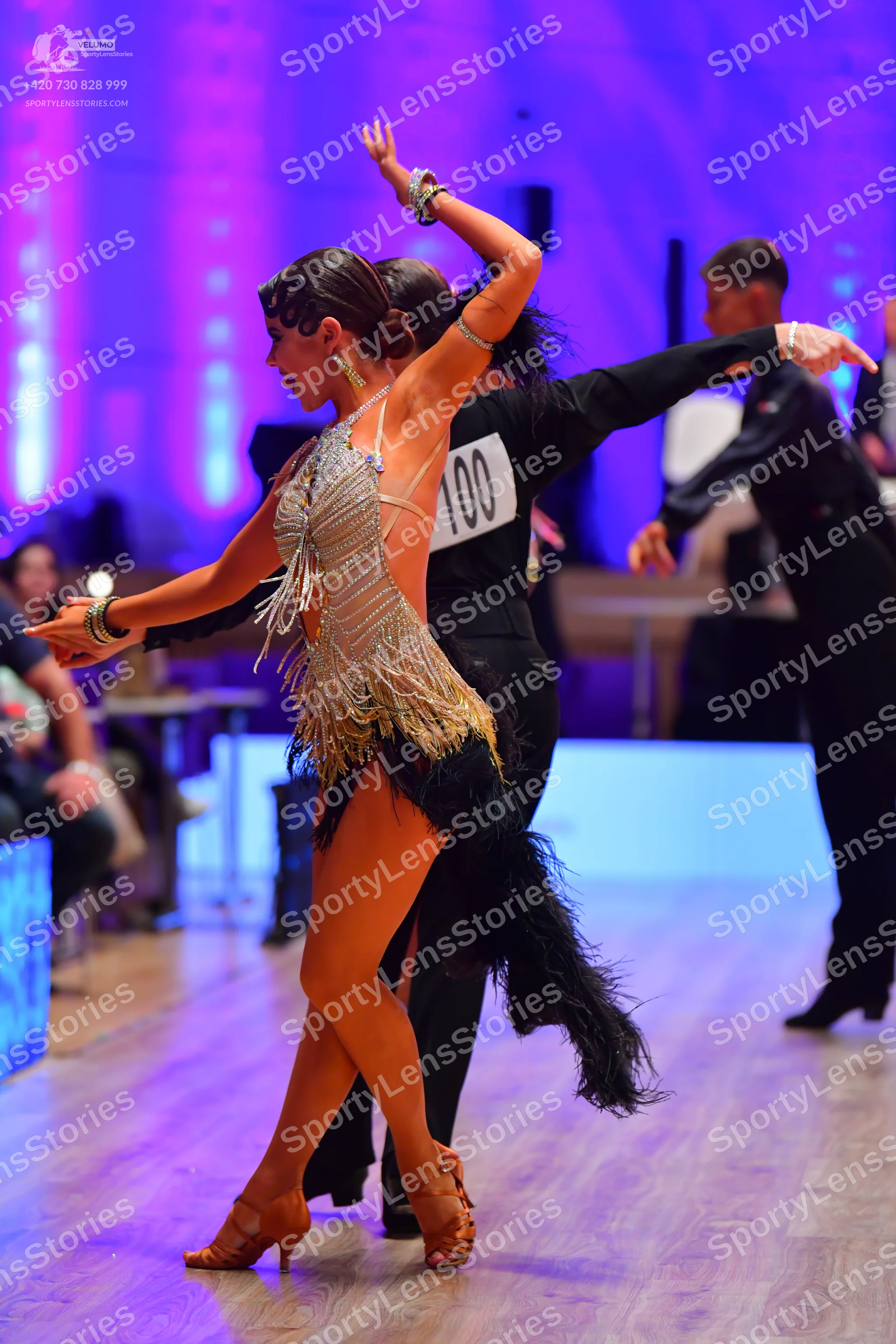 Dancesport competitor: Female dancer: gold latin dress with sequins and fringe, featuring black feather