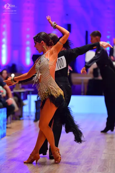 Dancesport competitor: Female dancer: gold latin dress with sequins and fringe, featuring black feather