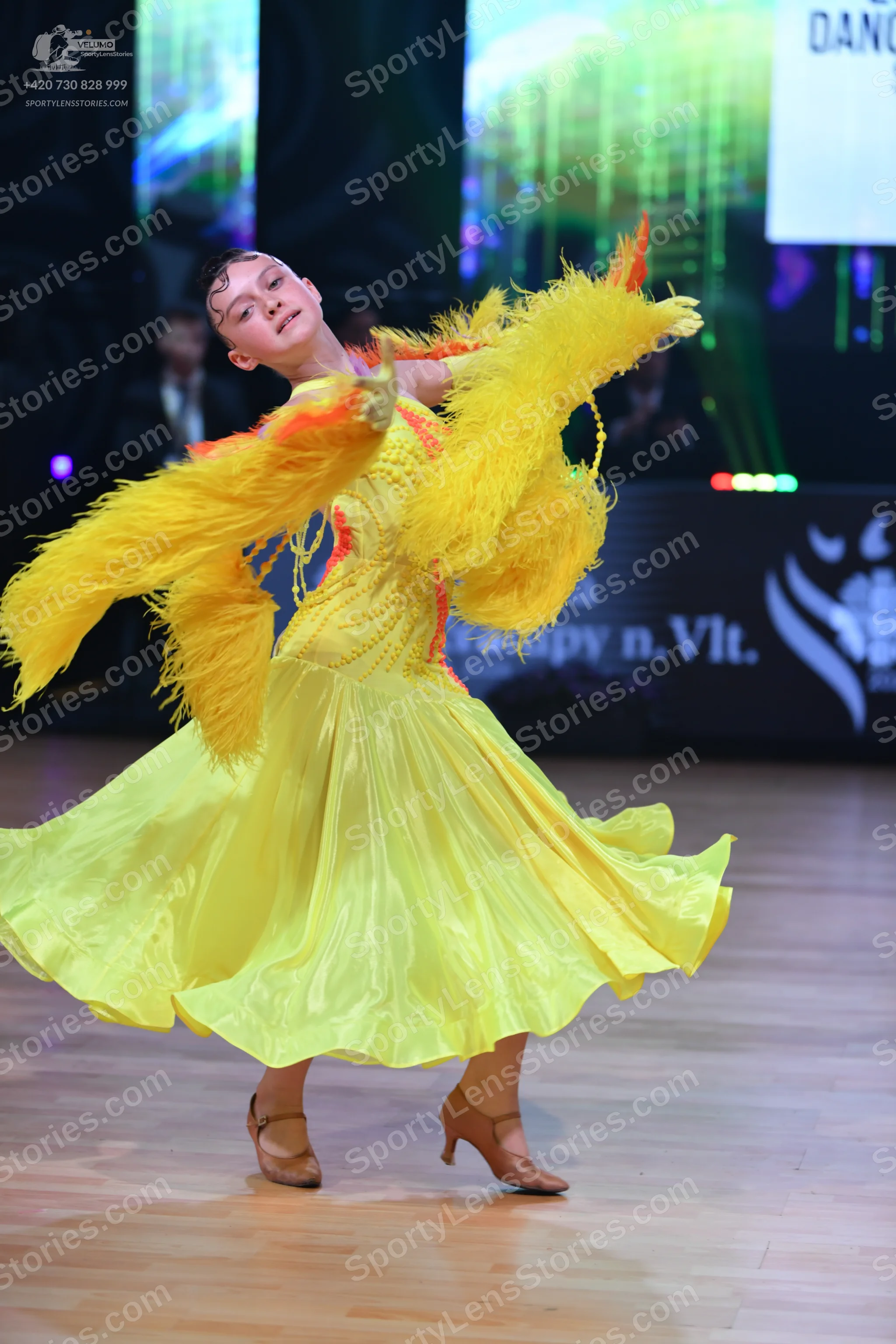 Dancesport competitor: Female dancer: yellow latin dress with large yellow feather sleeves and a flowin