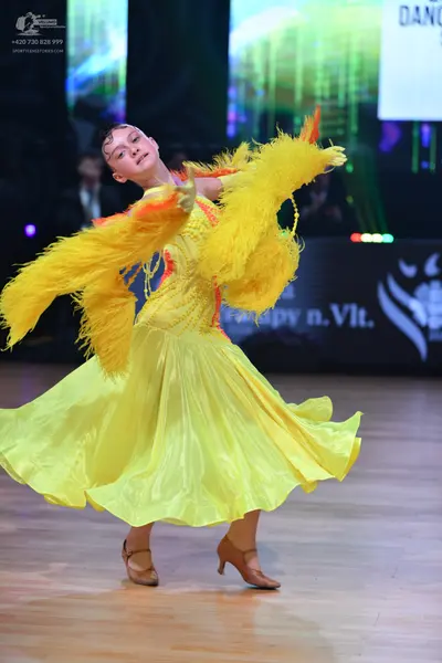 Dancesport competitor: Female dancer: yellow latin dress with large yellow feather sleeves and a flowin