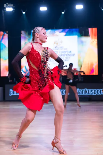 Dancesport competitor: Female dancer in foreground: red latin dress with sequins and ruffles, paired wi