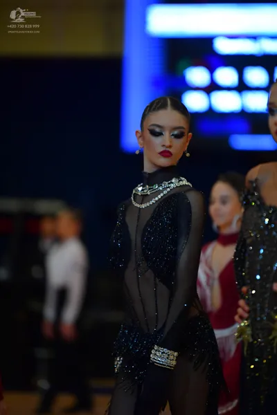 Dancesport competitor: Female dancer in foreground: black long-sleeved latin costume with sheer mesh, b