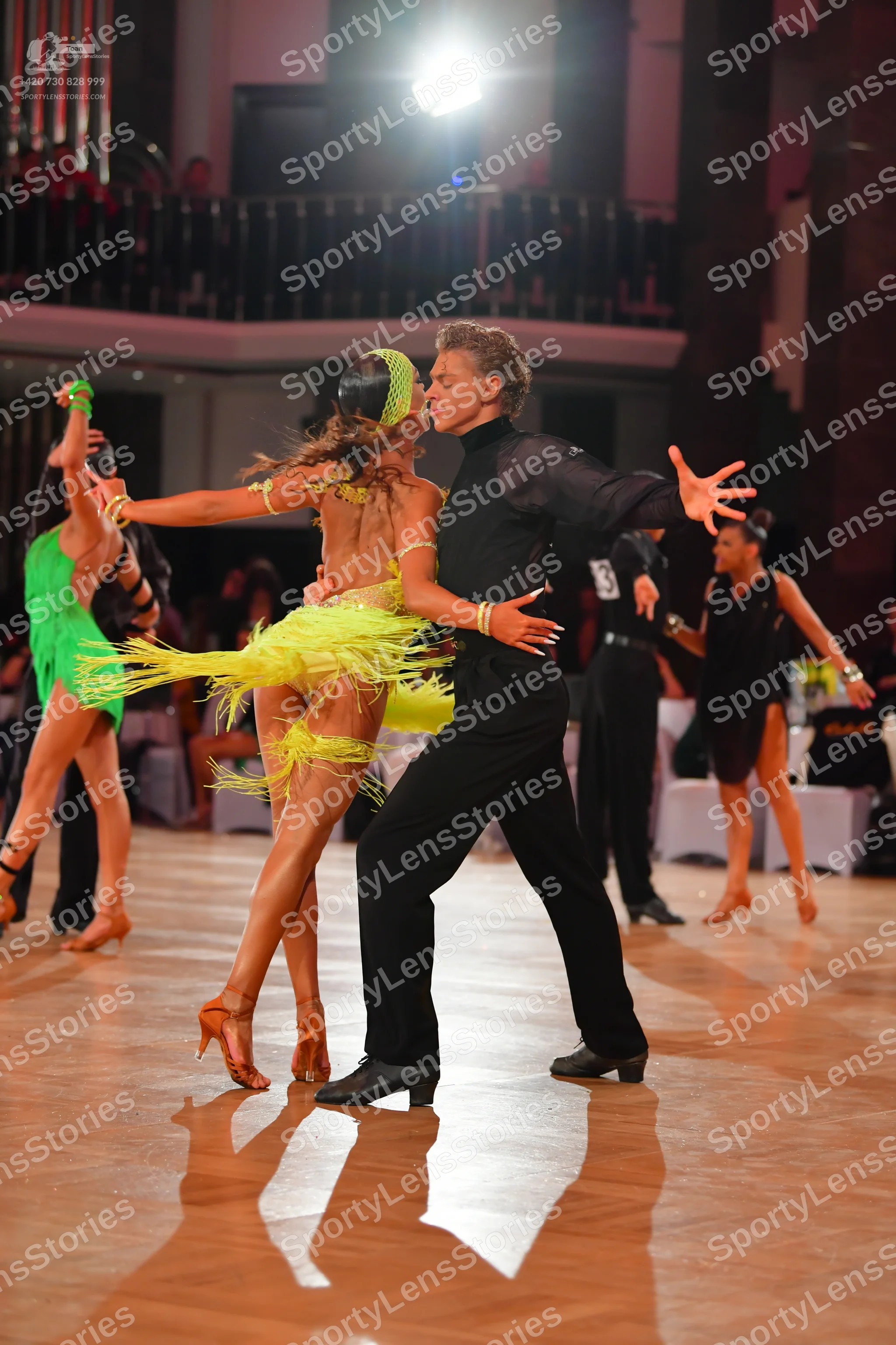 Dancesport competitor: Foreground female dancer: lime green Latin dress with heavy fringe and a sequine