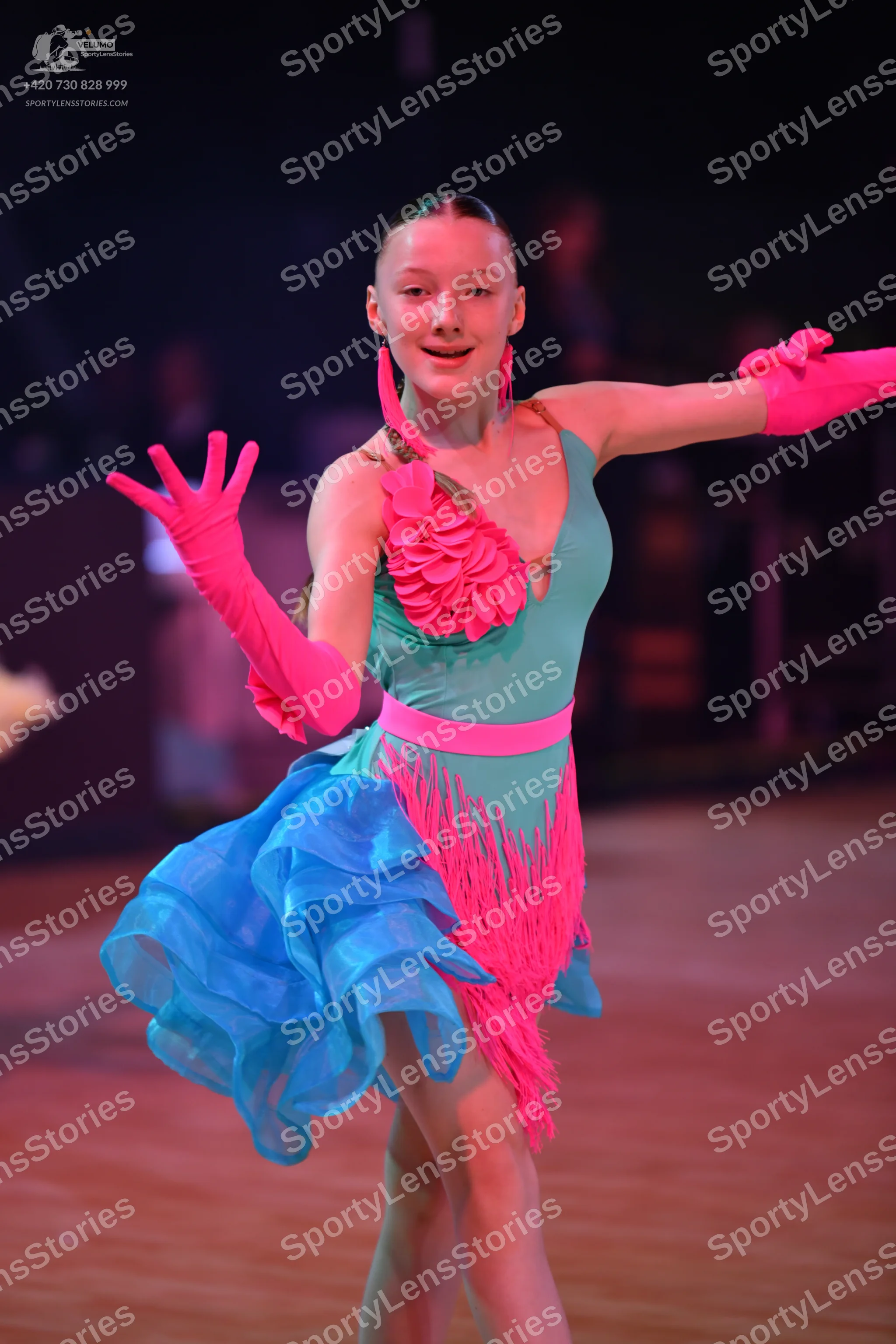 Dancesport competitor: Female dancer: teal Latin dance dress featuring bright pink floral ruffles on th
