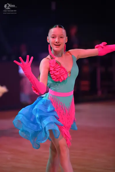 Dancesport competitor: Female dancer: teal Latin dance dress featuring bright pink floral ruffles on th