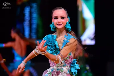 Dancesport competitor: Female dancer in foreground: teal and white Latin dance dress with large 3D teal
