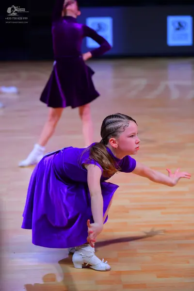 Dancesport competitor: Female dancer in background: dark purple long-sleeved A-line dress