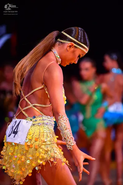 Dancesport competitor: Female dancer in foreground: yellow latin dress with many large gold/yellow sequ