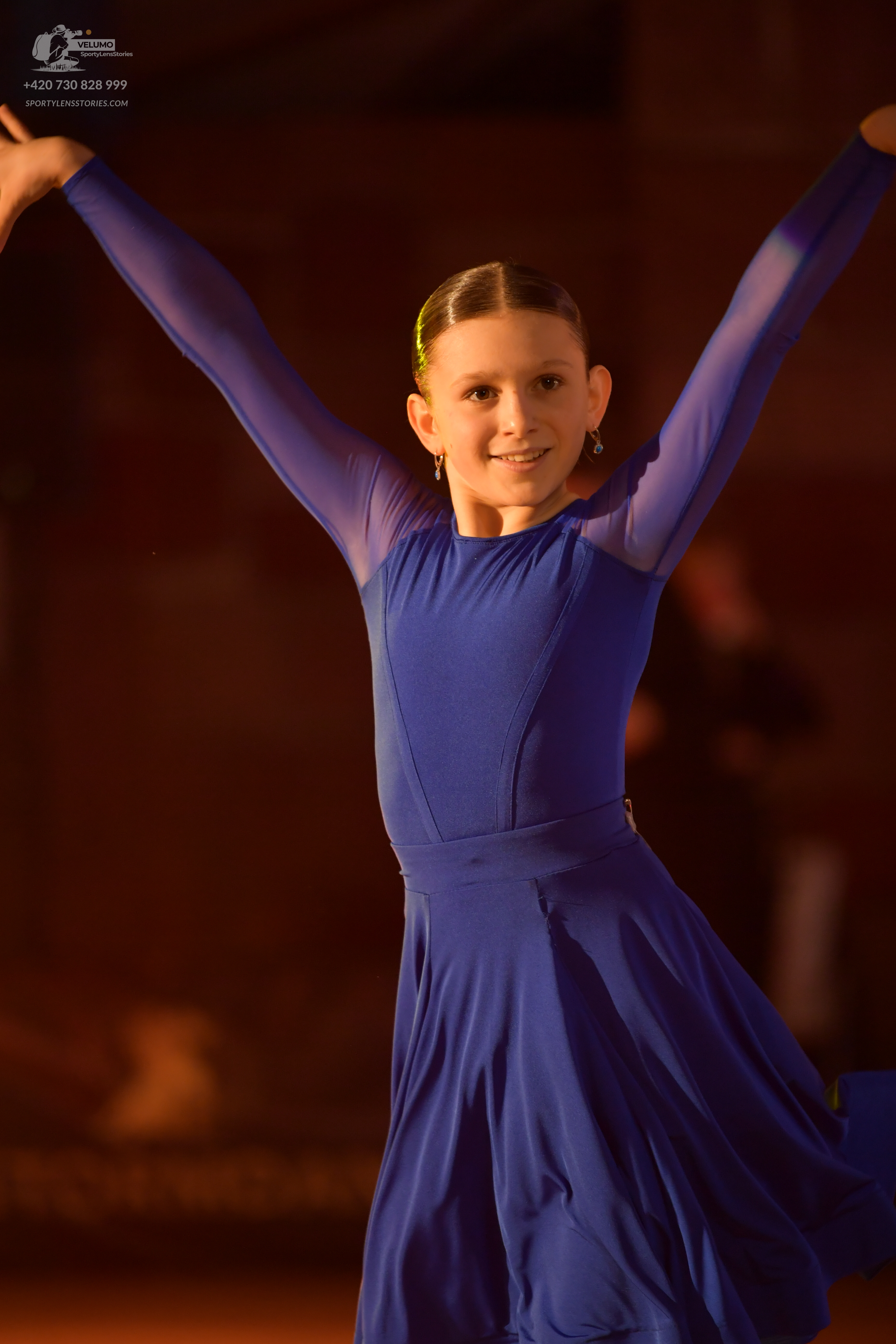 Dancesport competitor: Female dancer: long-sleeved royal blue ballroom dress with sheer mesh sleeves an