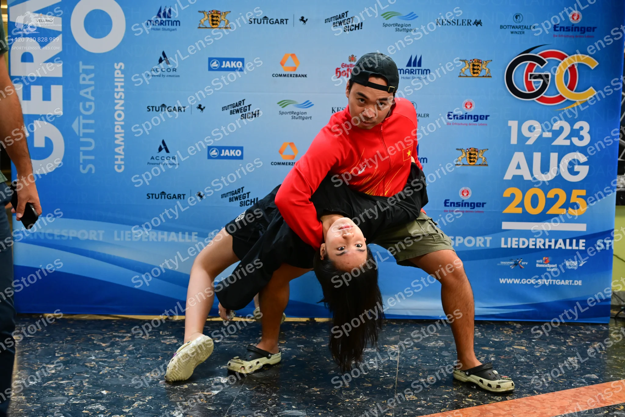 Dancesport competitor: Male dancer: red long-sleeved sweatshirt, black baseball cap, khaki shorts, and 