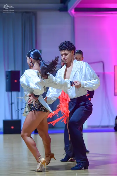 Dancesport competitor: Female dancer: white long-sleeved top, short sequined skirt, large black hoop ea