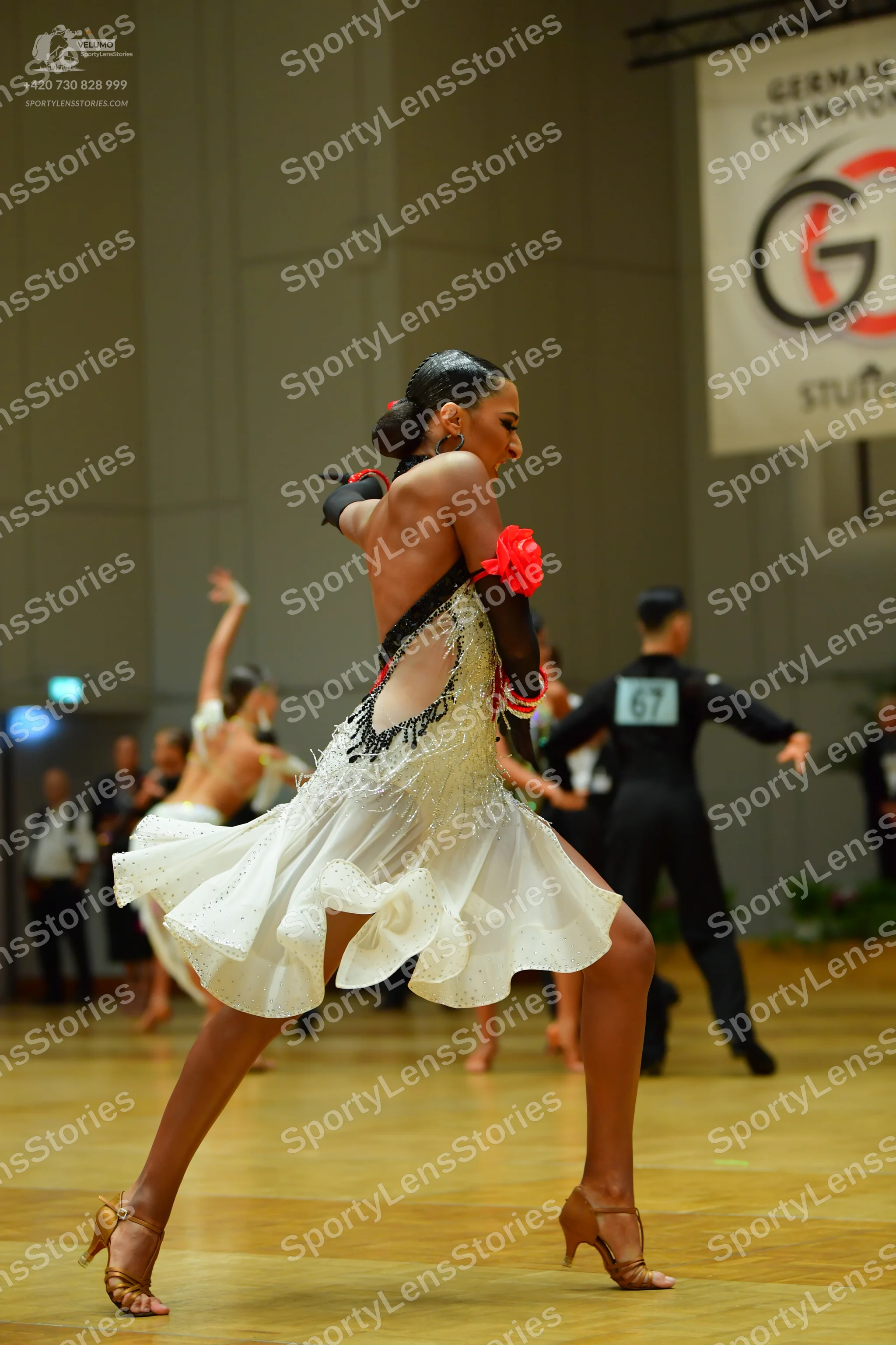 Dancesport competitor: Foreground female dancer: white latin dress with black lace/mesh details and a r