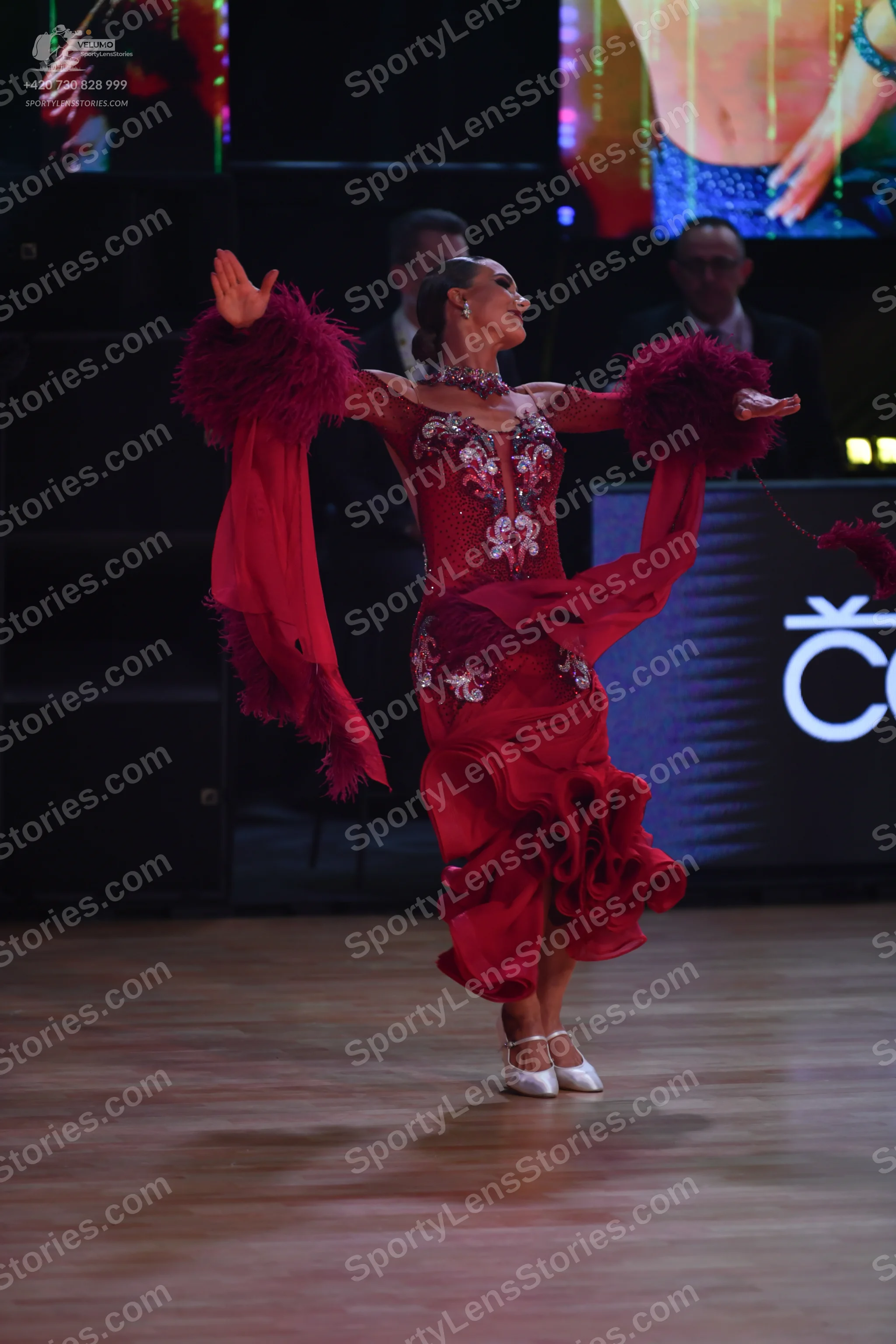Dancesport competitor: Female dancer: red Latin dress with a lace-detailed bodice, long flowing sleeves
