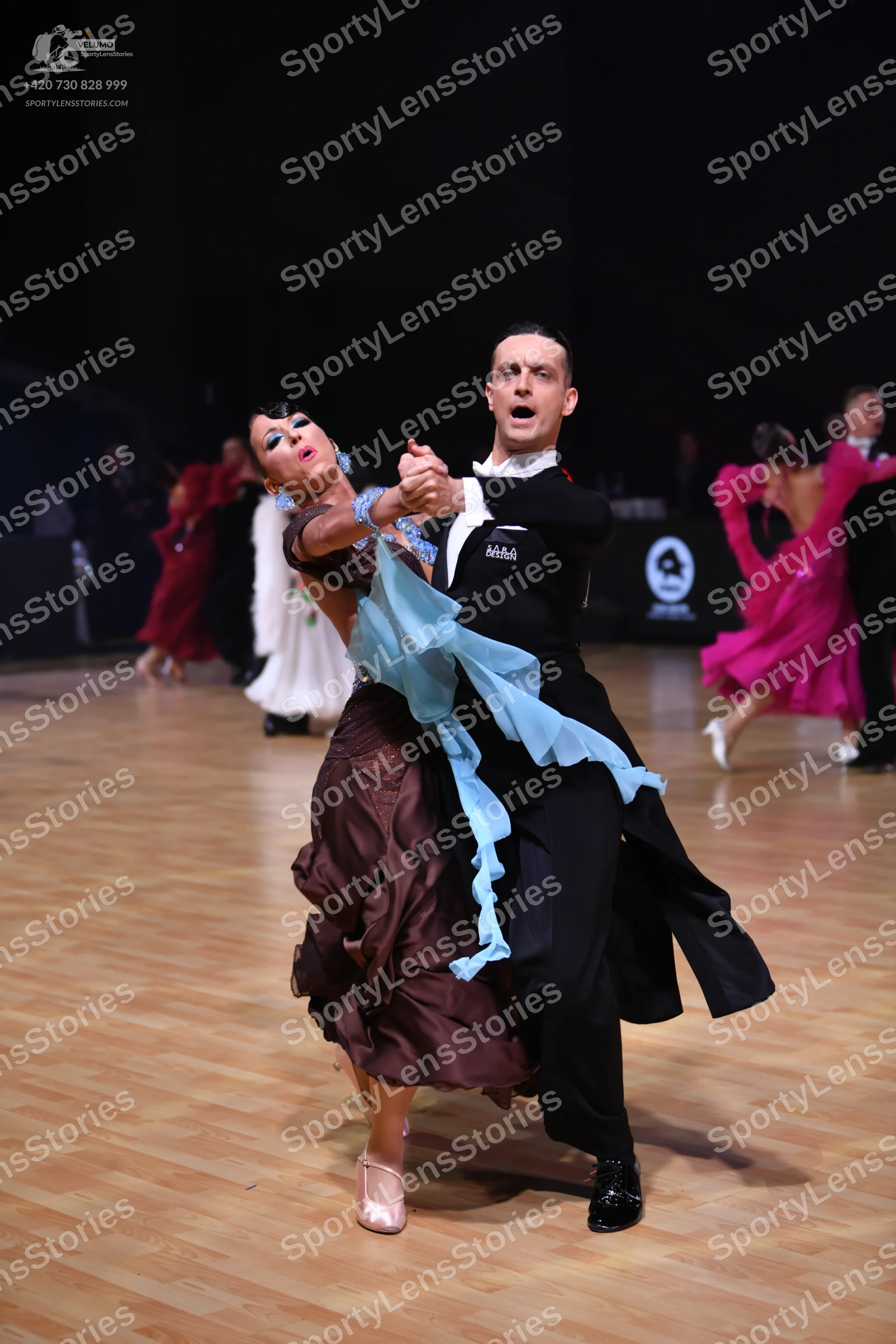 Dancesport competitor: Main female dancer: brown layered/ruffled skirt with a light blue sheer fabric t