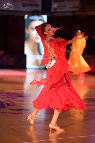 Dancesport competitor: Female dancer in foreground: red latin dress with flowing, layered fabric