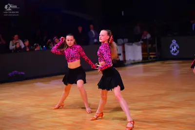 Dancesport competitor: Two female dancers wearing matching pink and black patterned long-sleeve crop to