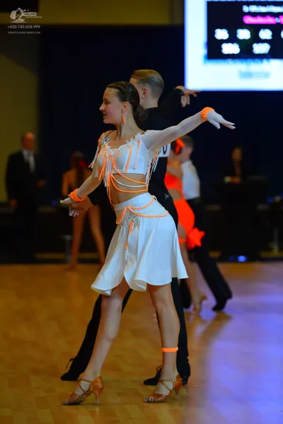 Dancesport competitor: Female dancer: white Latin dress with orange/peach-colored thin straps wrapping 