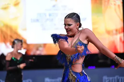 Dancesport competitor: Female dancer in foreground: blue and gold Latin dance costume featuring heavy b