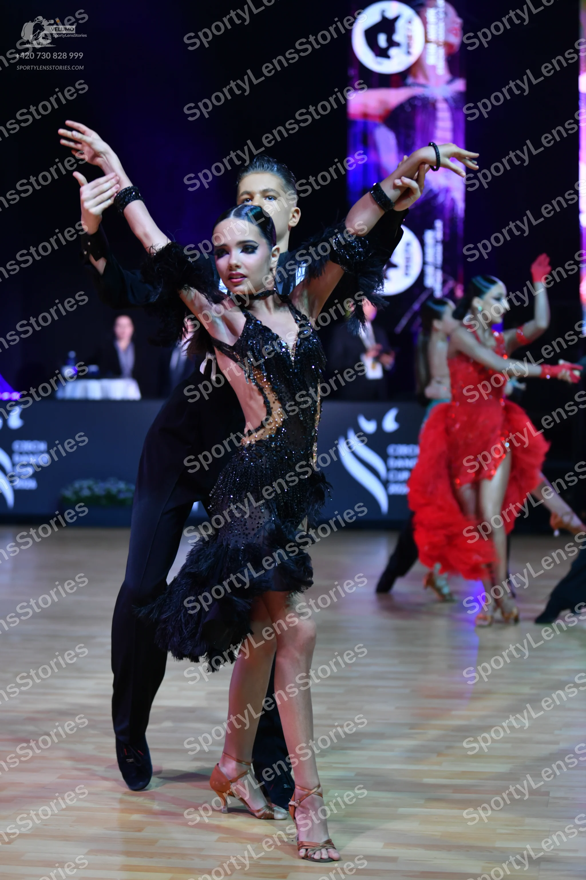 Dancesport competitor: Female dancer: black latin dress with sequins and a ruffled skirt, black wrist a