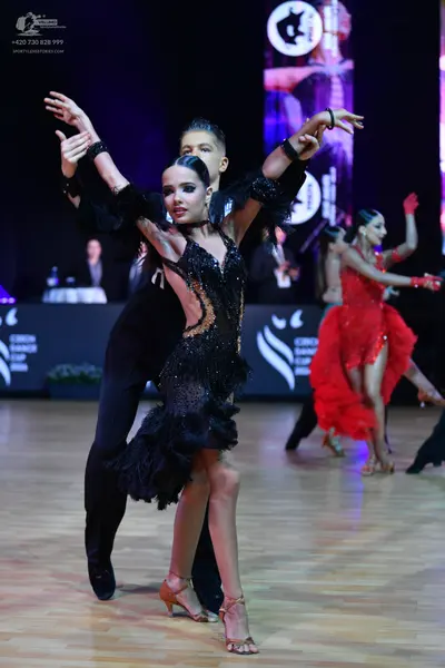 Dancesport competitor: Female dancer: black latin dress with sequins and a ruffled skirt, black wrist a