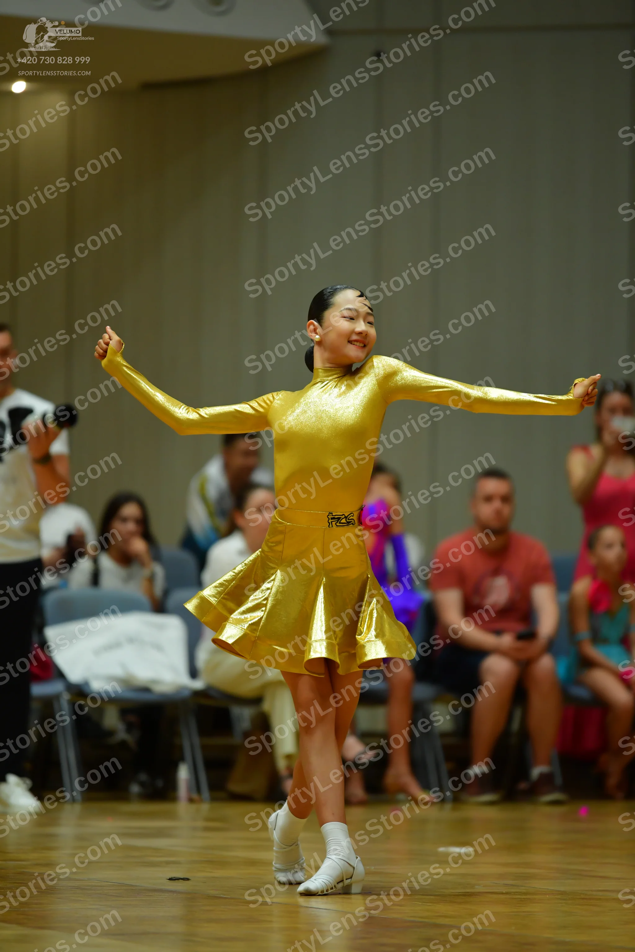 Dancesport competitor: Female dancer: gold metallic long-sleeved dress with a flared skirt and a decora