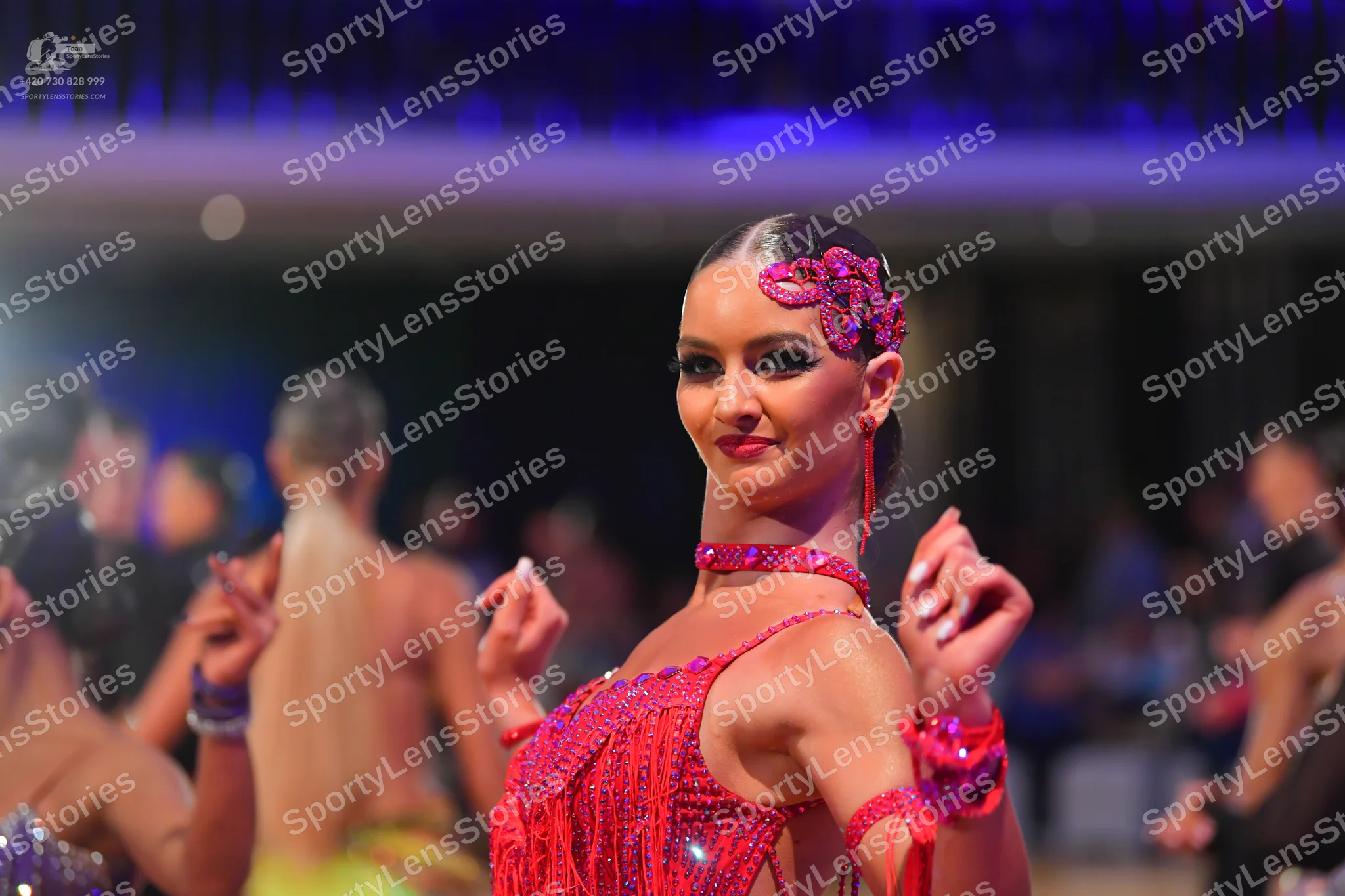 Dancesport competitor: Female dancer in foreground: red/pink Latin dress with sequins and fringe, inclu