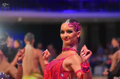 Dancesport competitor: Female dancer in foreground: red/pink Latin dress with sequins and fringe, inclu