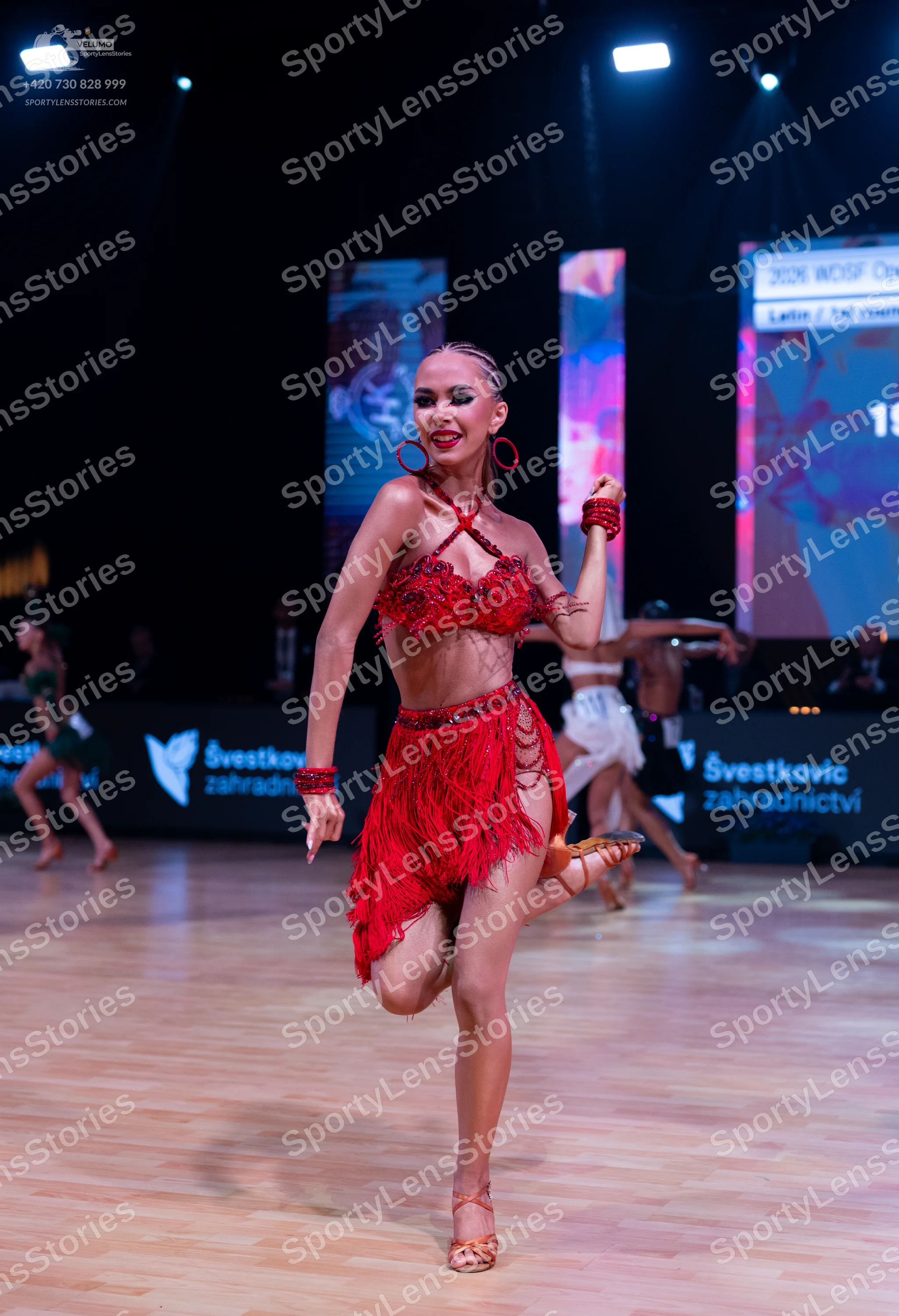 Dancesport competitor: Female dancer (foreground): red Latin dress with fringe and sequin/bead embellis