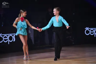 Dancesport competitor: Female dancer: light blue/cyan Latin-style dress with fringe/ruffles and a large