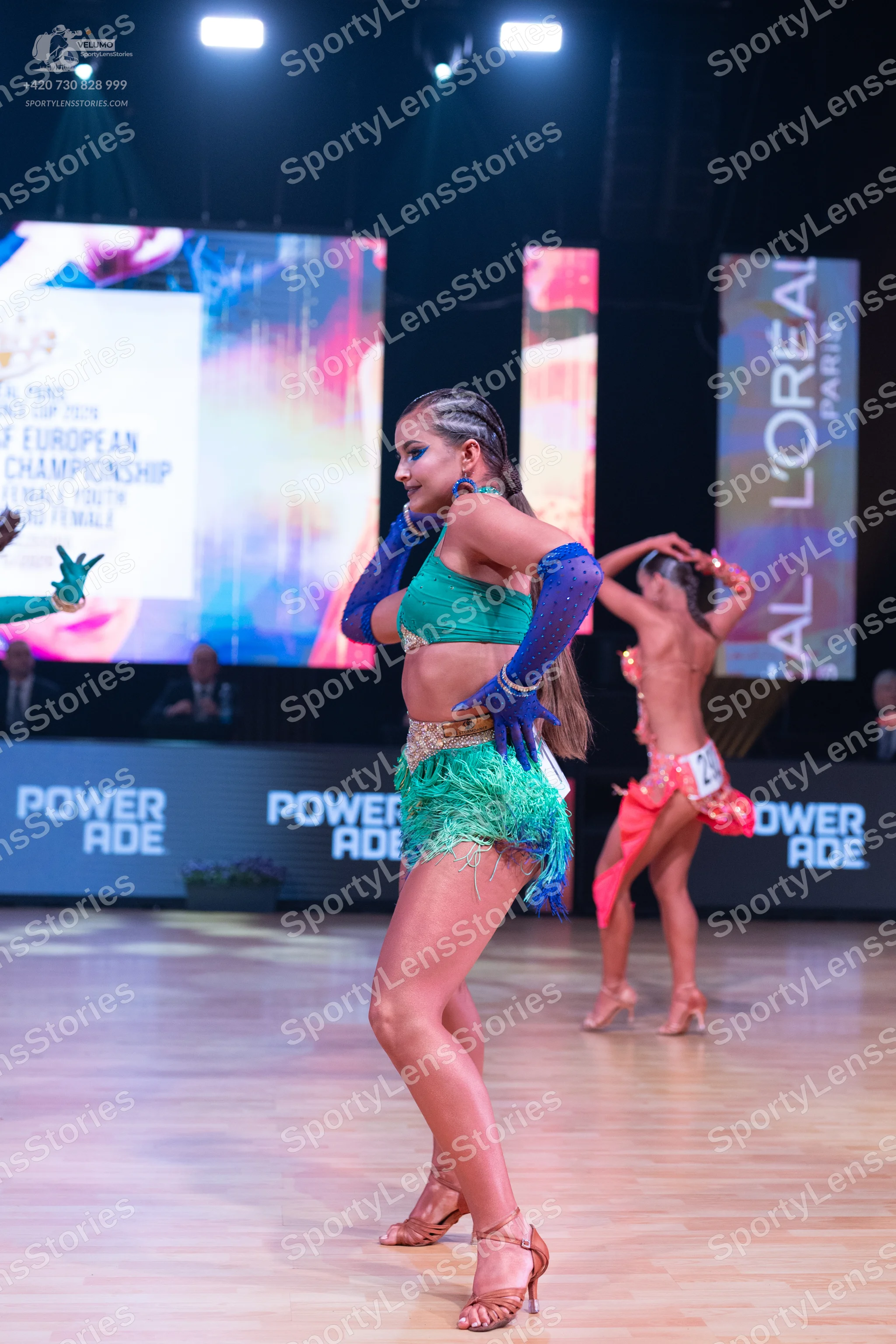 Dancesport competitor: Female dancer (foreground): teal Latin dance costume with a sequined top, a gree