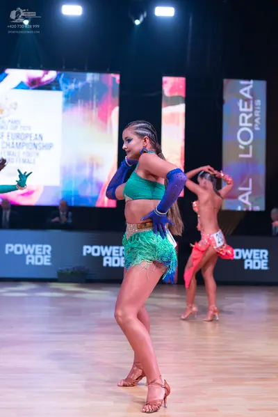 Dancesport competitor: Female dancer (foreground): teal Latin dance costume with a sequined top, a gree
