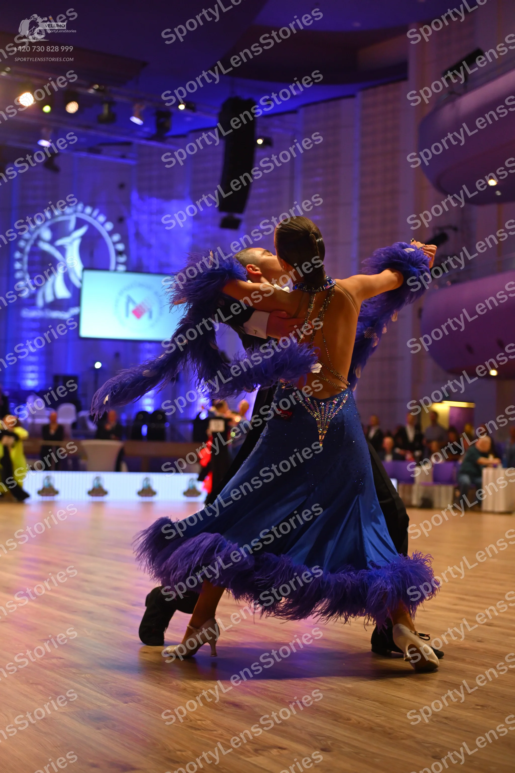 Dancesport competitor: Female dancer: blue latin dress with purple feathers and rhinestone embellishmen