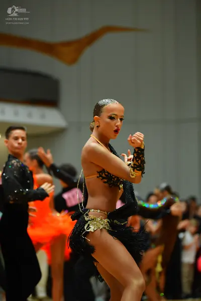 Dancesport competitor: Main female dancer: black Latin dance costume with intricate black lace, gold ac