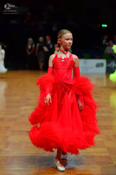 Dancesport competitor: Female dancer: red latin dress with a voluminous, ruffled skirt and matching arm