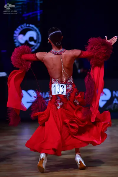 Dancesport competitor: Female dancer: red latin dress with feather/fringe accents on the sleeves and se