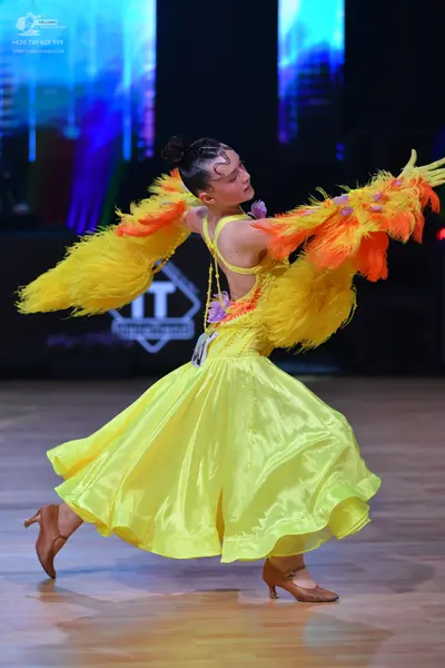 Dancesport competitor: Female dancer: bright yellow latin dress with large, voluminous yellow and orang