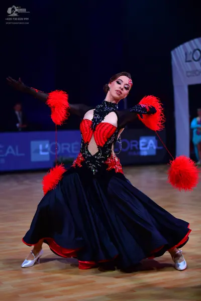 Dancesport competitor: Female dancer: black ballroom gown with red accents, featuring a black lace/sequ