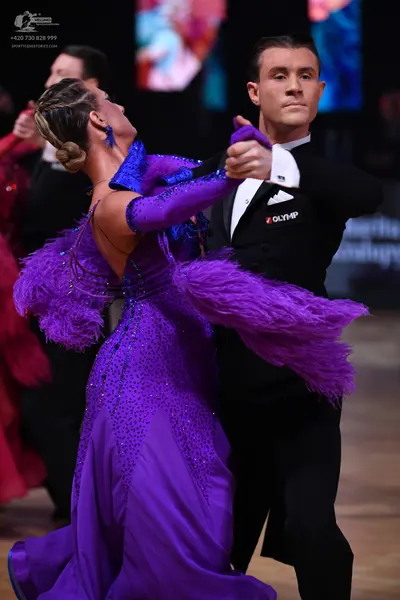 Dancesport competitor: Female dancer: purple ballgown with a sequined/beaded bodice, feather trim on th