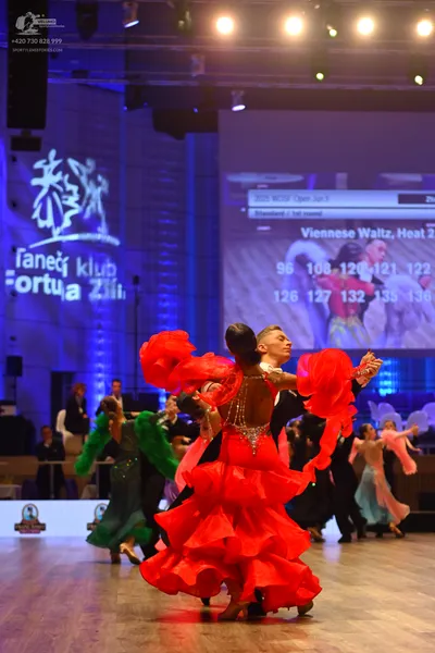 Dancesport competitor: Female dancer in foreground: red voluminous ballroom dress with many ruffled lay