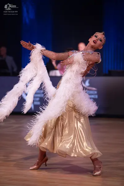 Dancesport competitor: Female dancer: gold metallic ballroom dress with large white feather accents on 