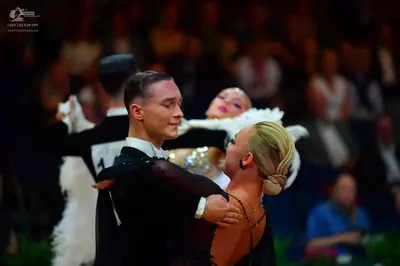 Dancesport competitor: Foreground male dancer: black long-sleeved dance shirt